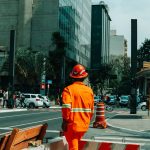 Trabalhador da construção civil em uma rua movimentada de São Paulo, cercado por pedestres e outros elementos da cidade.