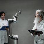 Dois pesquisadores trabalham juntos diante de um braço robótico em um laboratório de tecnologia.