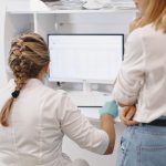 Dois profissionais de saúde trabalham diante de um computador em um ambiente hospitalar, analisando informações digitais.