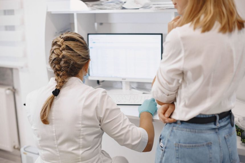 Dois profissionais de saúde trabalham diante de um computador em um ambiente hospitalar, analisando informações digitais.