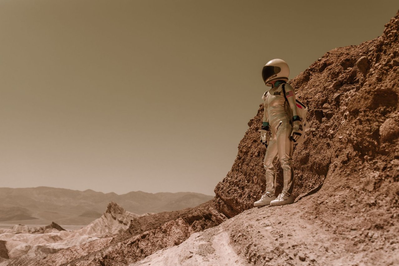 Astronauta em traje espacial sobre terreno rochoso semelhante à superfície de Marte.
