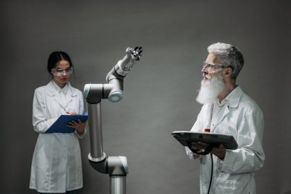 Dois pesquisadores trabalham juntos diante de um braço robótico em um laboratório de tecnologia.