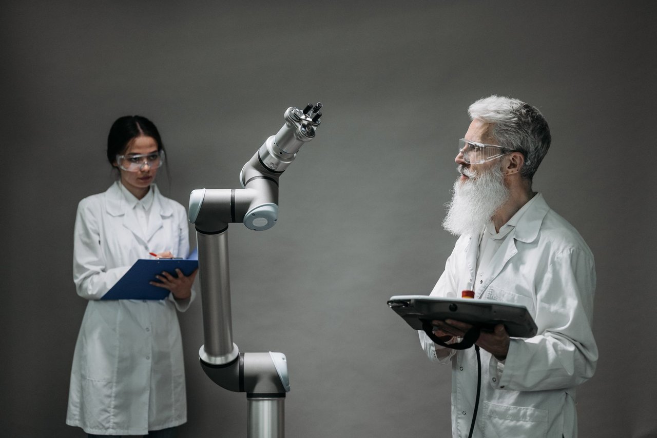 Dois pesquisadores trabalham juntos diante de um braço robótico em um laboratório de tecnologia.